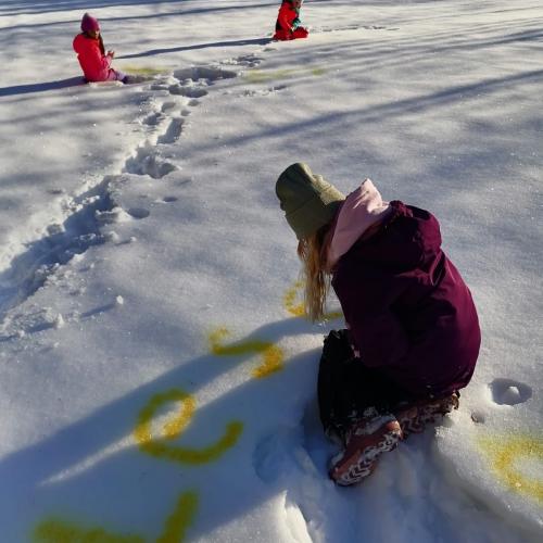 Kind beim Schreiben des Wortes "Lesen" mit gelber Sprühfarbe im Schnee