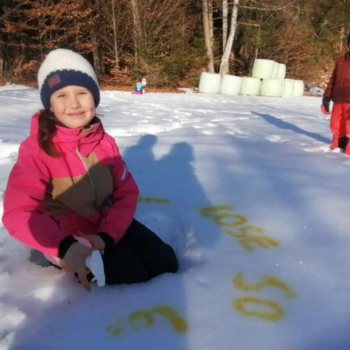 Mädchen, das lächelnd beim Sprühen mit gelber Sprühfarbe im Schnee in die Kamera blickt