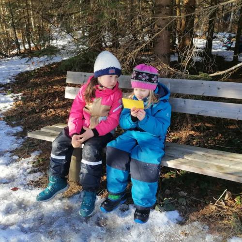 zwei Mädchen, die mit einer gelben Lesekarte gemütlich auf einer Bank sitzen