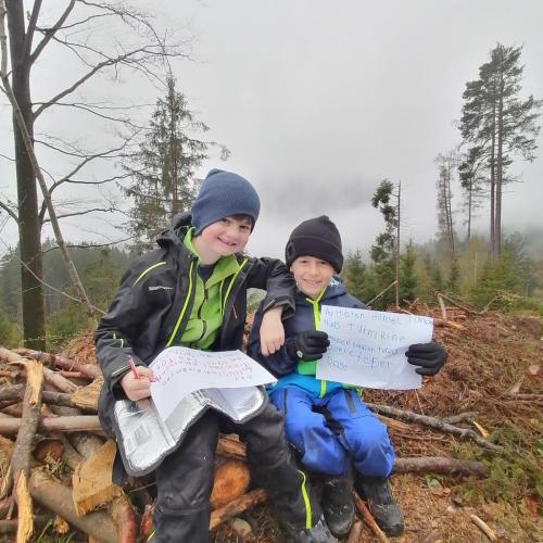 2 Kinder präsentieren stolz ihre geschriebenen Sätze während sie auf umgeknickten dünnen Bäumen sitzen